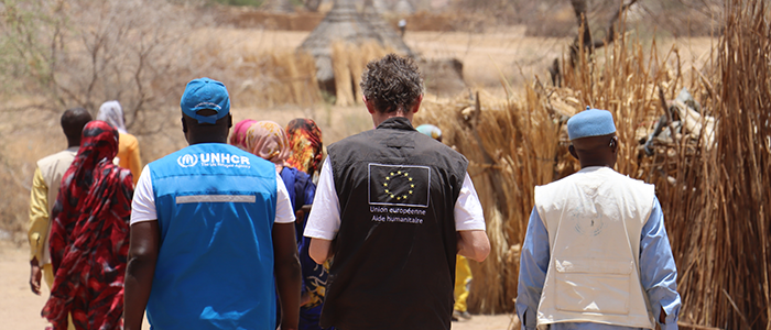 A group of three humanitarian experts. The one of the left wears an UNHCR vest, the one in the middle wears and EU vest, and the one on the right wears a beige vest. They are in Chad while working in the arrival of Sudanese refugees.