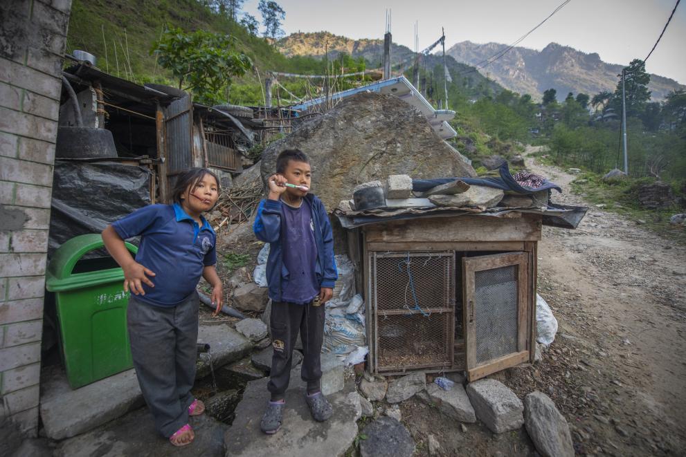 Children getting ready for a new day in an area prone to regular landslides. A boy is brushing his teeth outside while his sister stands by.