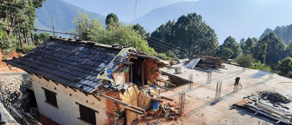 View of a damaged house, trees and hills in the background.