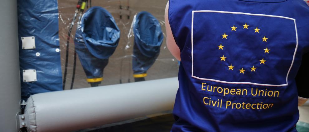 Person seen from the back, the EU Civil Protection shown, standing in front of a desinfection tent.