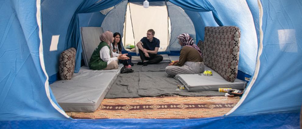 View of people sitting in a shelter tent, the entrance is shown in the foreground