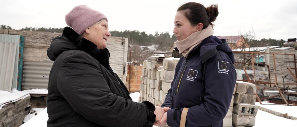 A woman holding hands with an aid worker in a garden covered with snow.