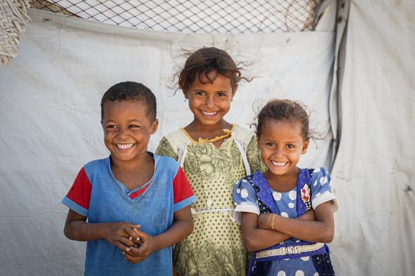 Photo of 3 children standing in front of a refugee tent