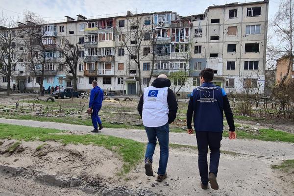 EU humanitarian aid staff looking at destroyed appartment building