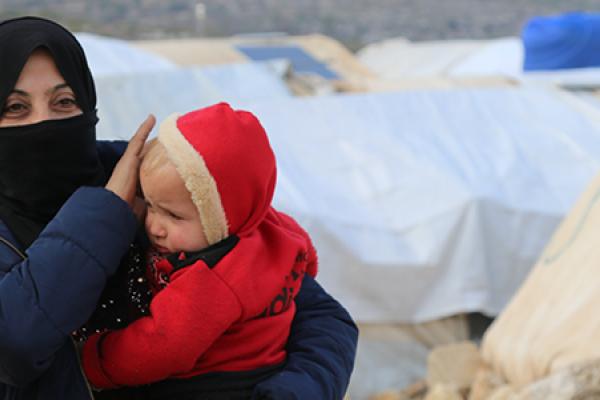 Woman holding child in her arms with on the background a refugee camp