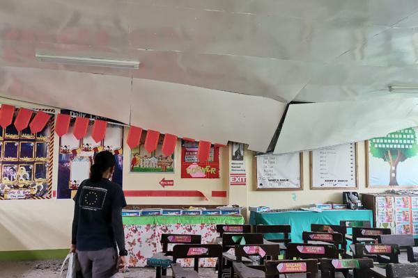 Aid worker looking at a collapsed roof inside a classroom