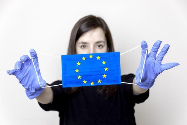 Woman wearing gloves holding a face mask decorated with an EU flag