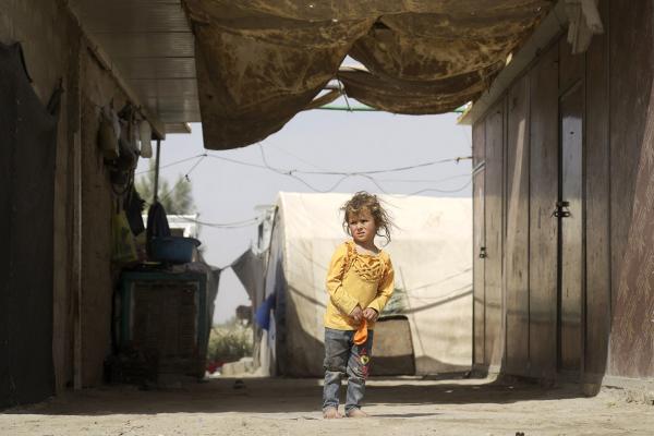 Girl standing underneath a makeshift roof in front of shelter tents.