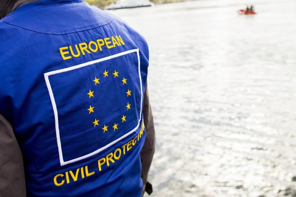 View of a lake, in the foreground an aid worker carrying a vest with the european emblem.