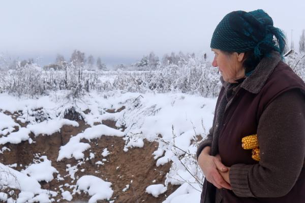 A woman standing in a snowy landscape holding corn under her arm.