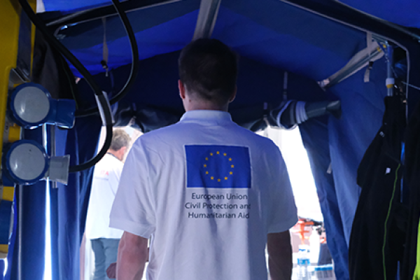 View from inside a field hospital to outside. In the doorway a person wearing a white t-shirt with the EU flag printed on it.