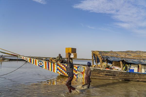 View of a colorful boat on the river. Goods are being unpacked by 2 persons.
