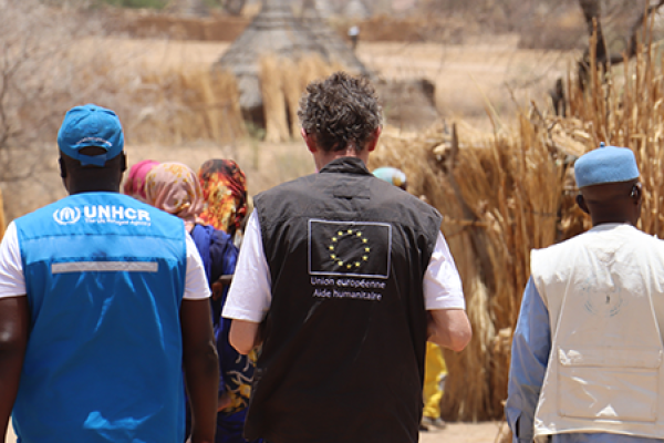 A group of three humanitarian experts. The one of the left wears an UNHCR vest, the one in the middle wears and EU vest, and the one on the right wears a beige vest. They are in Chad while working in the arrival of Sudanese refugees.