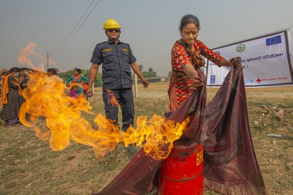 A women putting out a fire in a barrel with a blanket. In the background a firefighter/trainer.