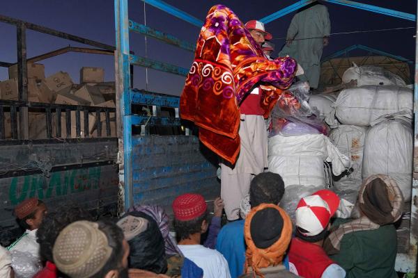 Bags with goods being distributed from a truck. People eagerly awaiting in front.
