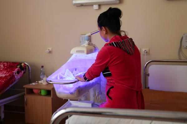 A woman, seen from the back, next to an incubator.