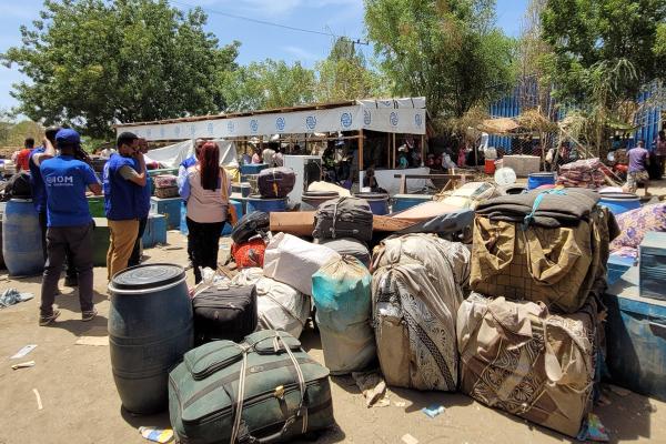 View of piles of luggage in the background people trying to cross the border.