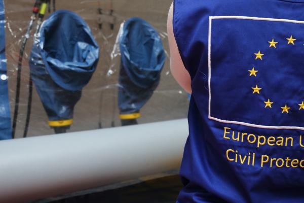 Person seen from the back, the EU Civil Protection shown, standing in front of a desinfection tent.
