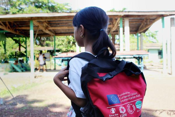 A girl carrying a small back pack walking towards a school building.
