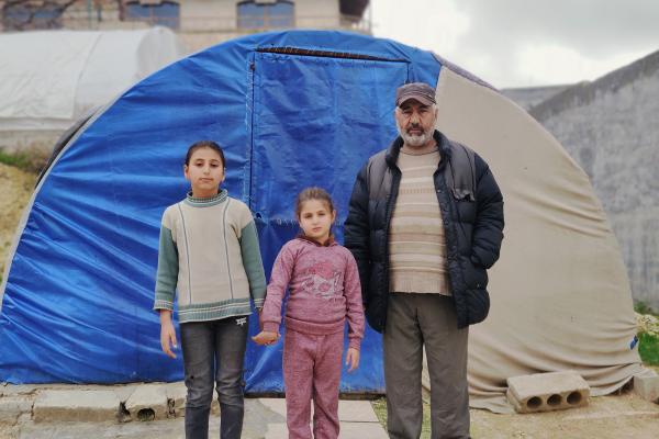 Rafiq with his daughters in front of a tent.