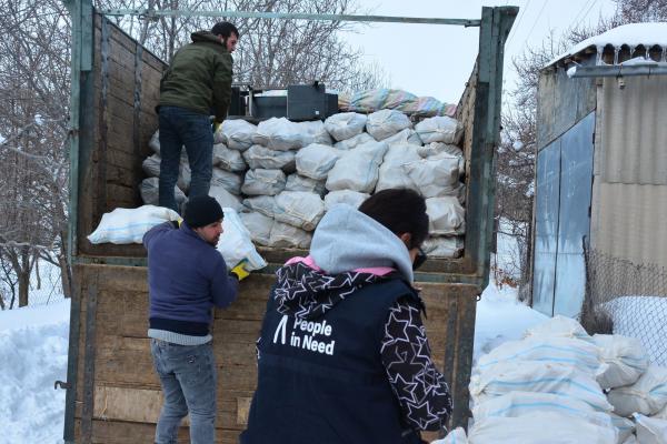 People unloading goods from a truck standing in a street covered with snow.
