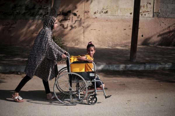A woman pushing a girl in a wheel chair in a street seen from the side.
