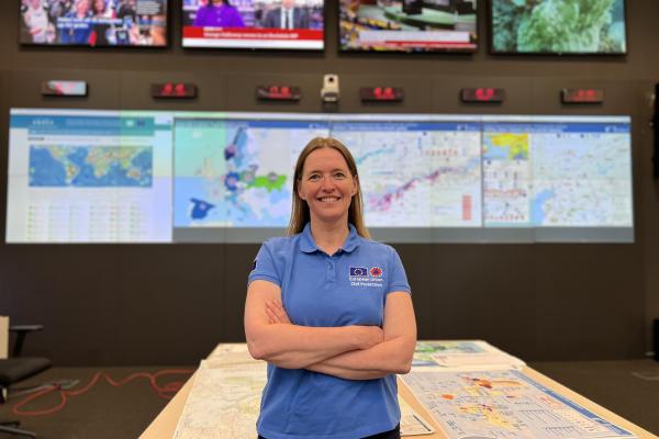 Claire in the EU’s Emergency Response Coordination Centre in Brussels, large screens displaying maps and news channels in the background.