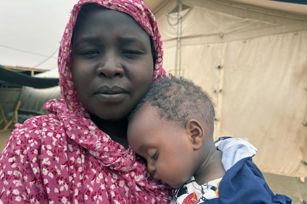 Saad holding her 9-month-old daughter in her arms, standing in front of a tent.